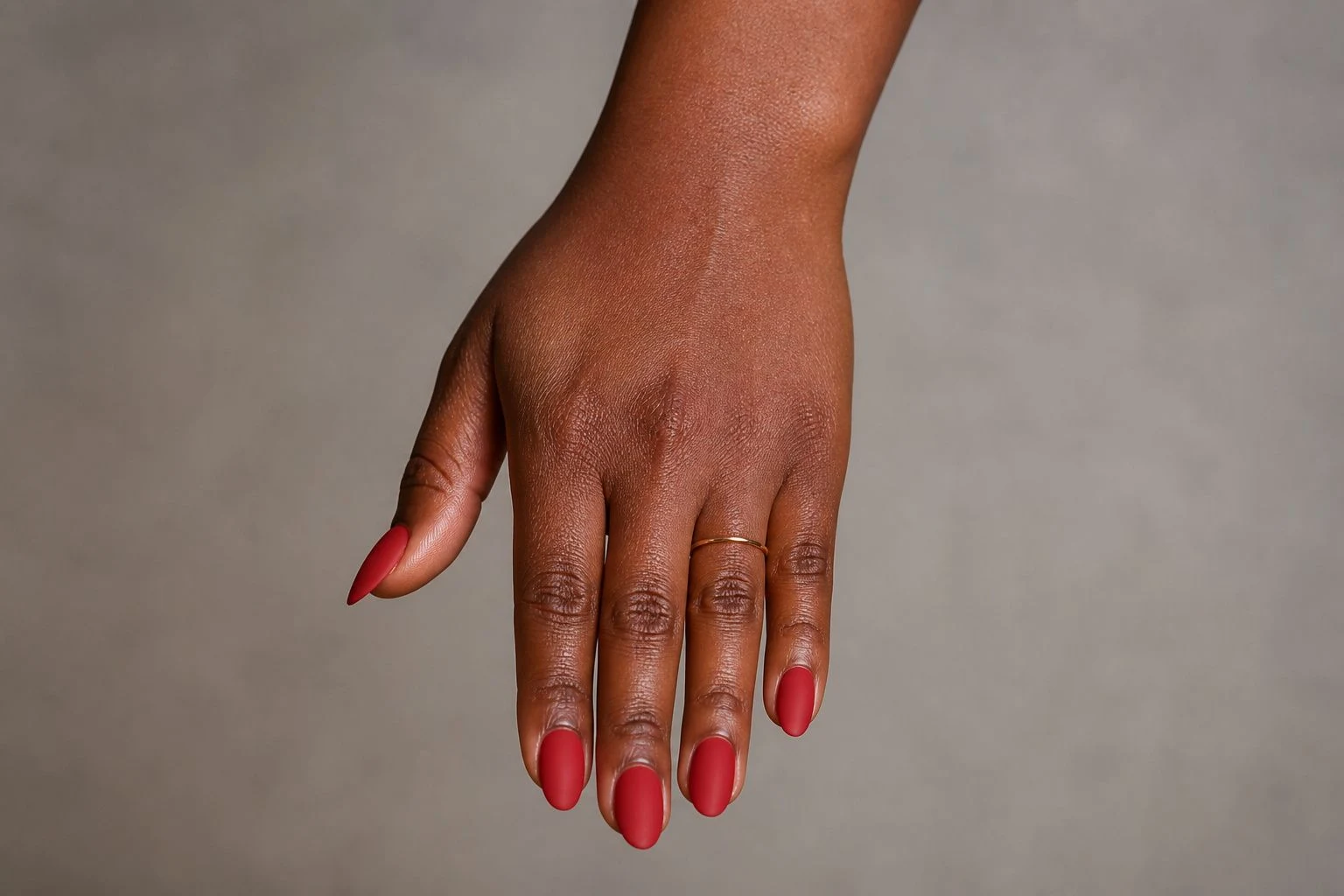 Matte red almond Christmas nails with the wrist turned forward and a delicate gold ring