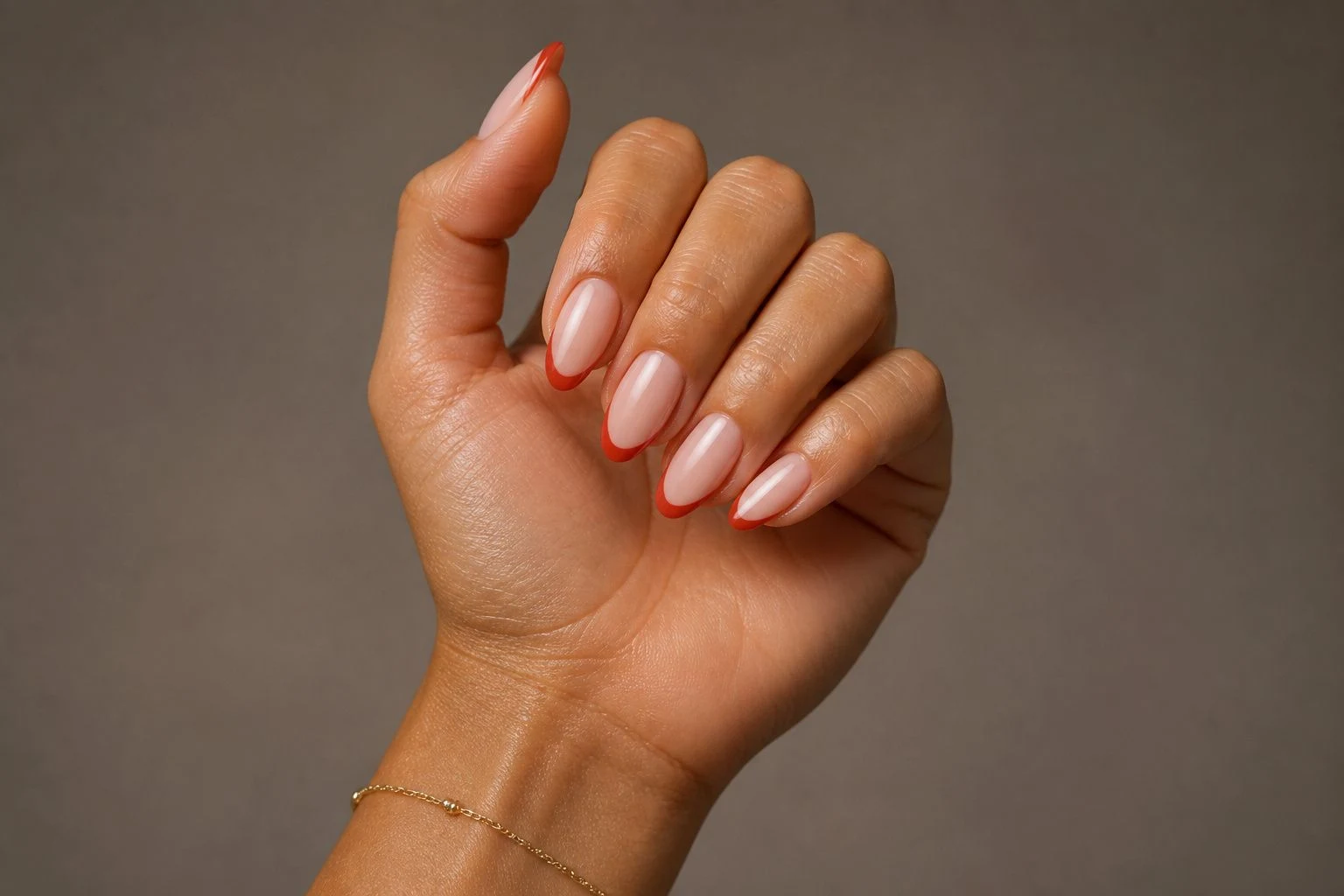 Red French almond Christmas nails in a curled hand pose with a delicate gold bracelet