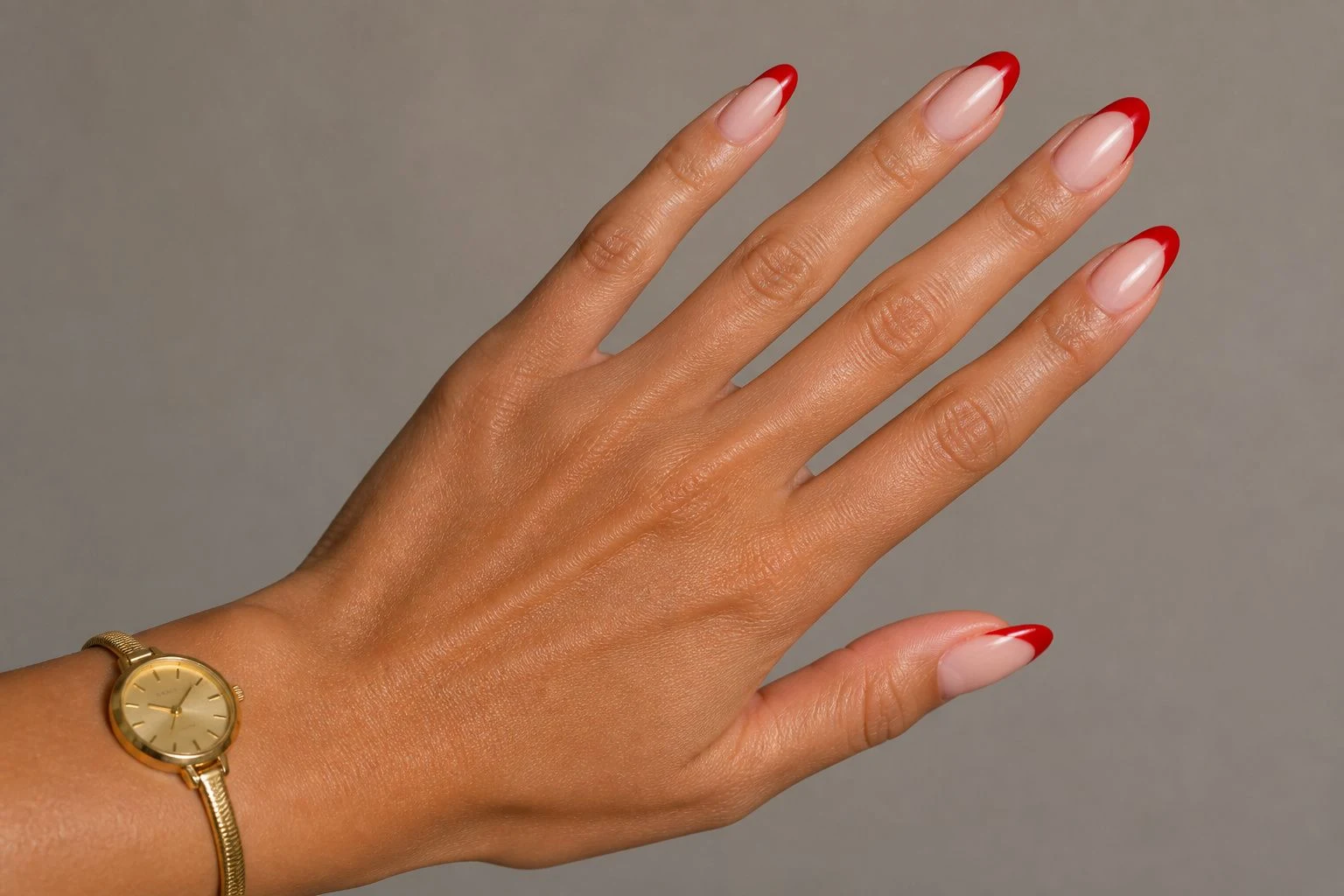 Red French tip Christmas nails in a natural fan hand pose with a delicate gold watch