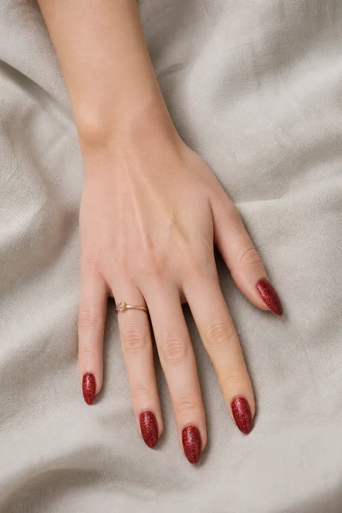 fine ruby red glitter almond nails on a light warm hand with visible wrist and forearm