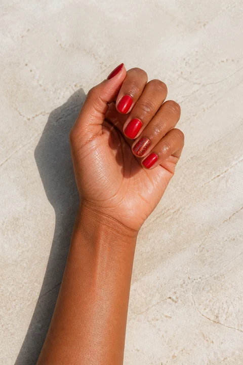 glossy red nails with one fine glitter accent on a warm brown hand with visible wrist