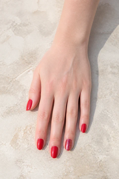 red nails with ruby glitter on the thumb and little finger of a deep brown hand with visible wrist and forearm
