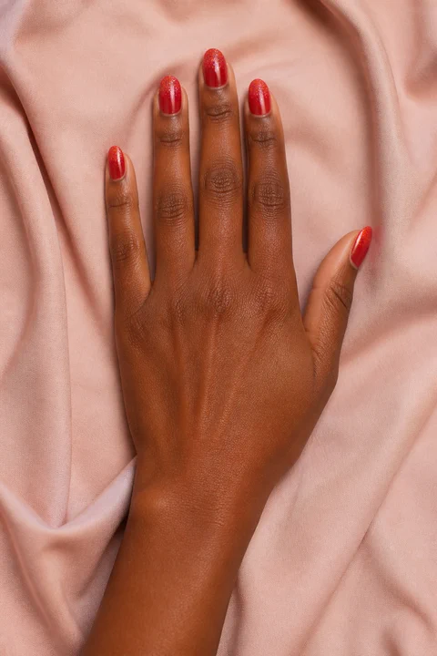 fine ruby glitter fading from the tips of red almond nails on a light golden hand with visible wrist and forearm