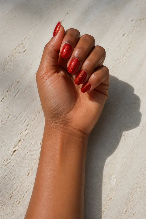 bright red glitter party nails on a rich deep skin tone hand with visible wrist