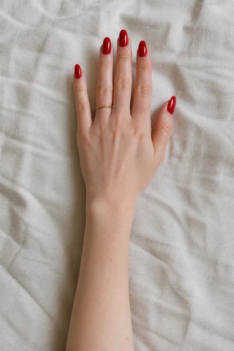 glossy classic cherry red almond nails on a light warm hand with visible wrist and forearm
