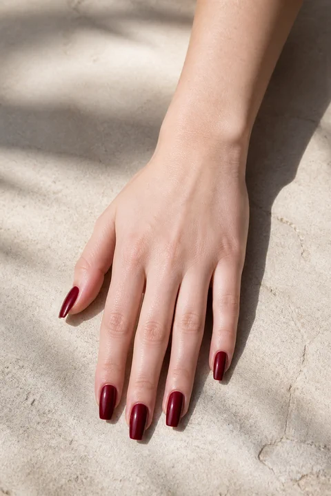 soft rounded tomato red nails on a deep brown hand with visible wrist and forearm