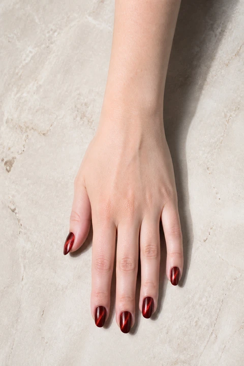 garnet red nails with a glowing magnetic velvet finish on a dark brown hand with visible wrist and forearm