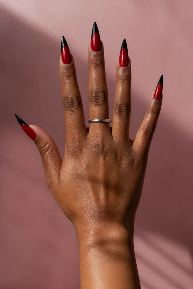 red and black French stiletto nails on a deep brown hand with fingers spread in soft daylight
