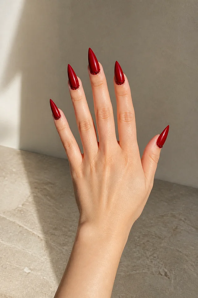 red glossy stiletto nails on a fair hand angled over a light surface with visible wrist