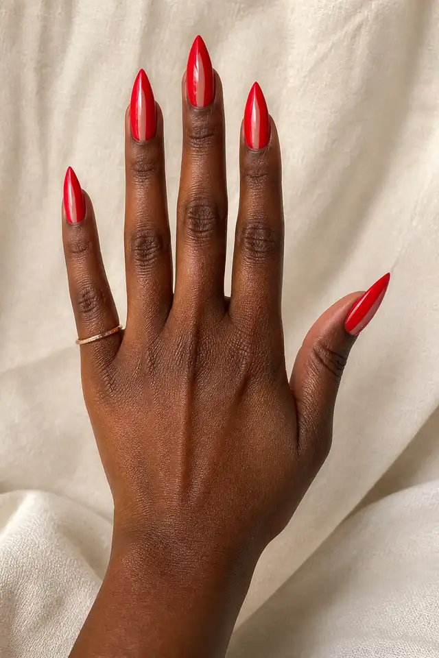 red glossy stiletto nails on a deep brown hand posed over white fabric in natural window light