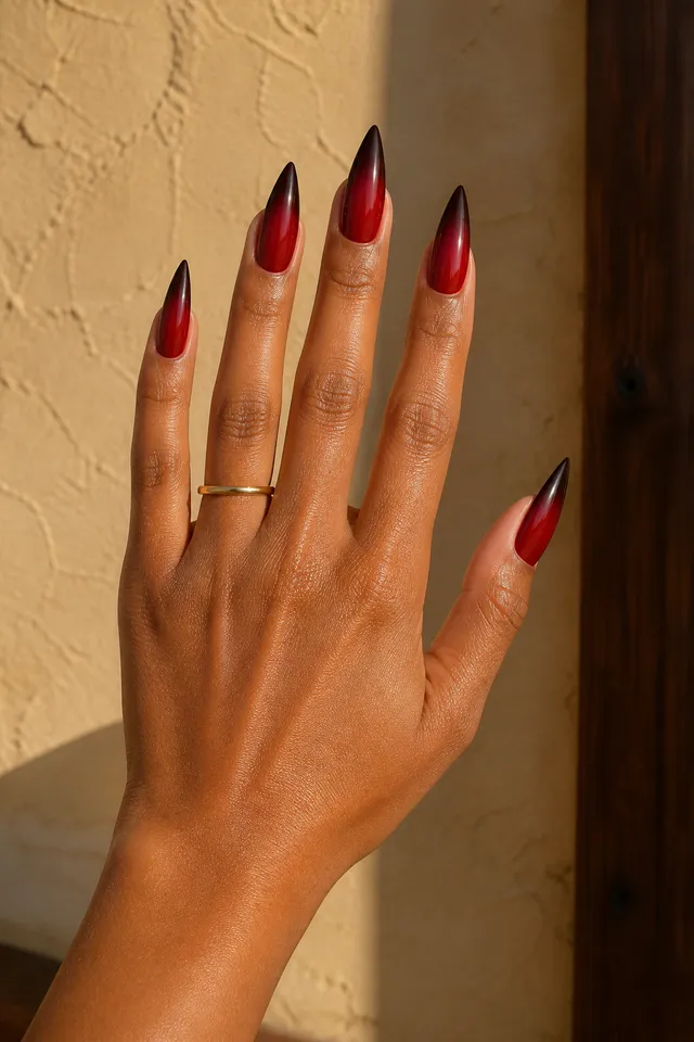 deep red and black ombre stiletto nails on a warm brown hand with fingers spread in daylight