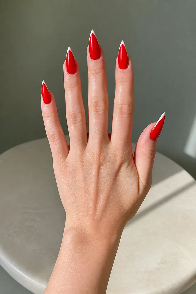 bright red glossy stiletto nails on a fair hand resting on a white round surface with visible wrist