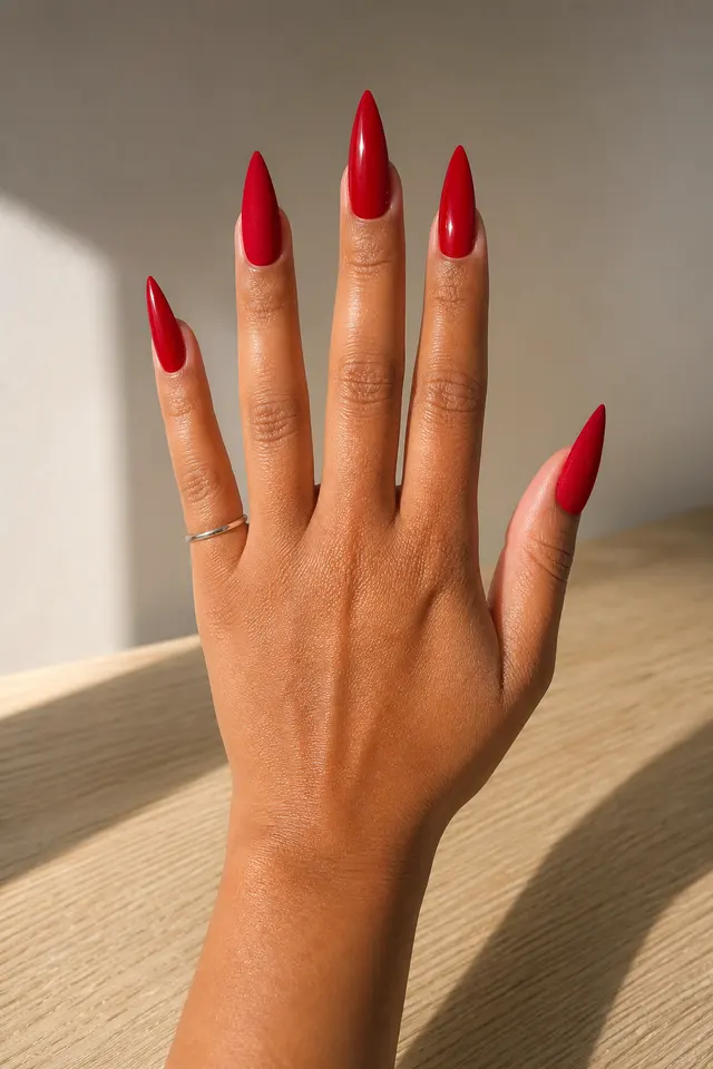 red glossy stiletto nails on a medium tan hand with fingers spread over a wood surface in daylight