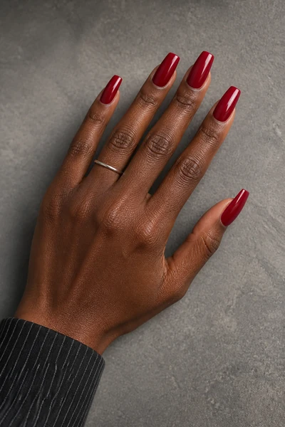 Deep ruby red coffin nails on a deep brown skin tone hand in a fingertip-rest pose with visible wrist and short partial forearm, natural daylight