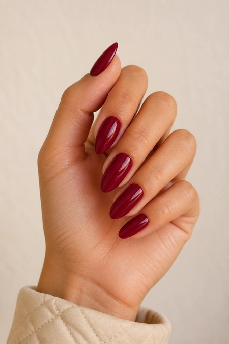 Deep wine red almond nails on a tan skin tone hand in a gentle pinch pose with visible wrist and short partial forearm, natural daylight