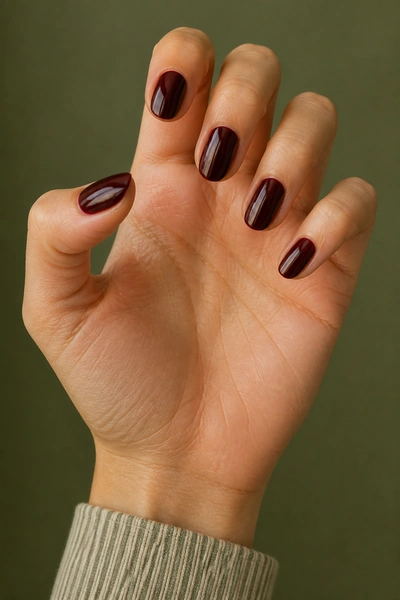 Black cherry red short oval nails on a light olive skin tone hand in a relaxed open palm angle with visible wrist and short partial forearm, natural daylight