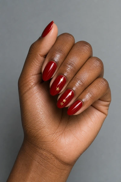 Red nails with delicate gold star accents on a deep brown skin tone hand in a side angled display with visible wrist and short partial forearm, natural daylight