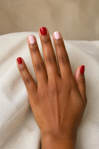 Alternating red and blush short rounded square nails on a medium deep skin tone hand in a palm-down three-quarter pose with visible wrist and short partial forearm, natural daylight