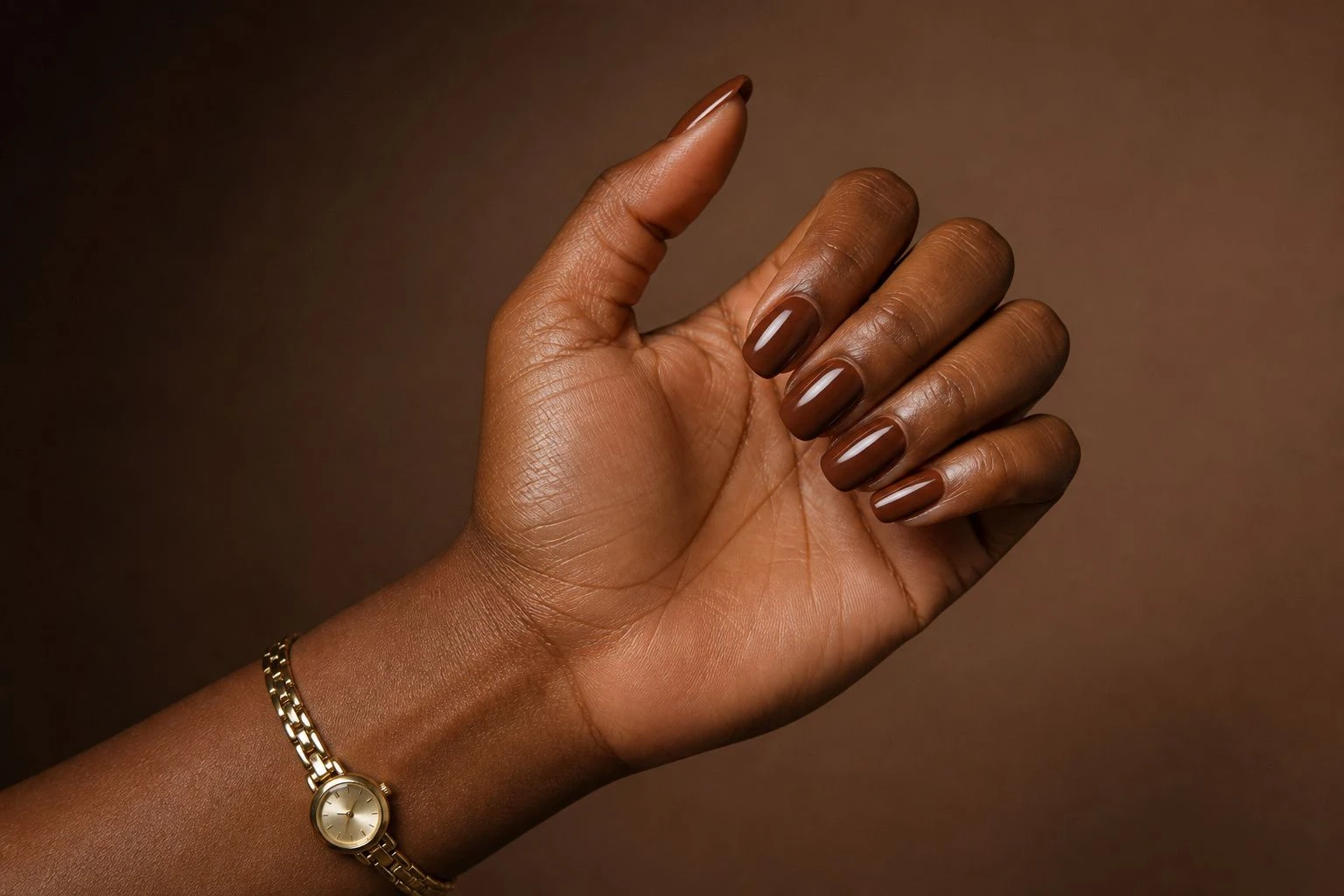 Short glossy almond shaped cocoa brown manicure with a slim gold watch, simple Christmas nail idea