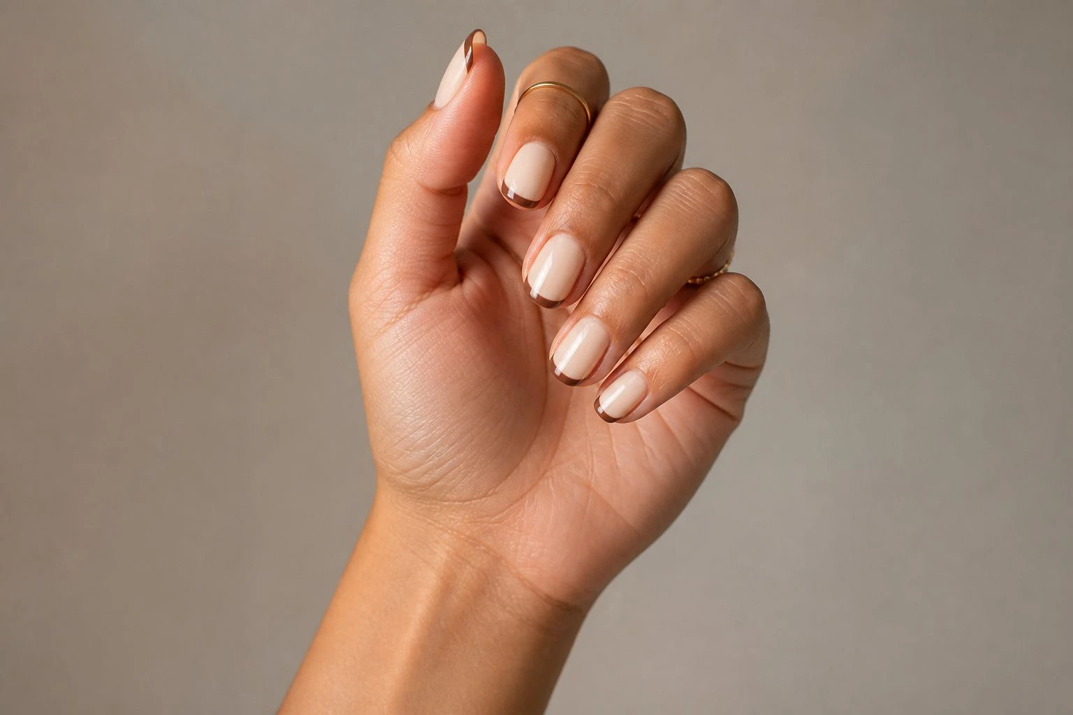 Short oval cream base with cocoa brown French tip manicure and two delicate gold rings, simple Christmas nail idea