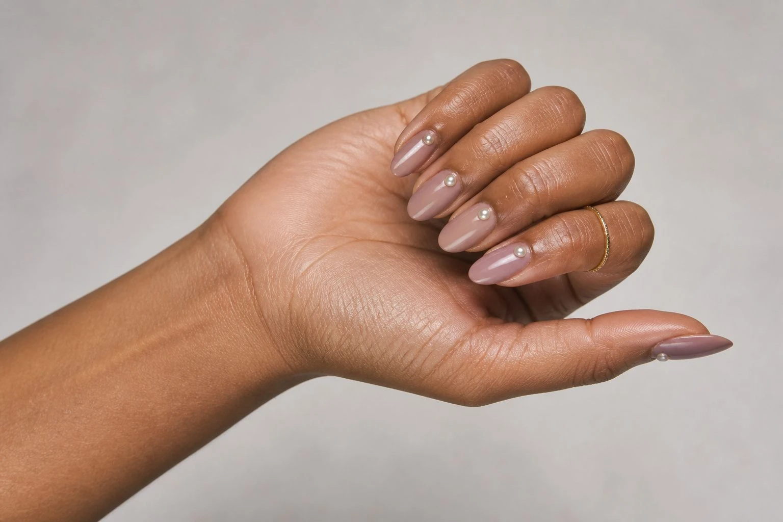 Short glossy almond soft mauve nude manicure with a pearl dot accent and a gold ring, simple Christmas nail idea