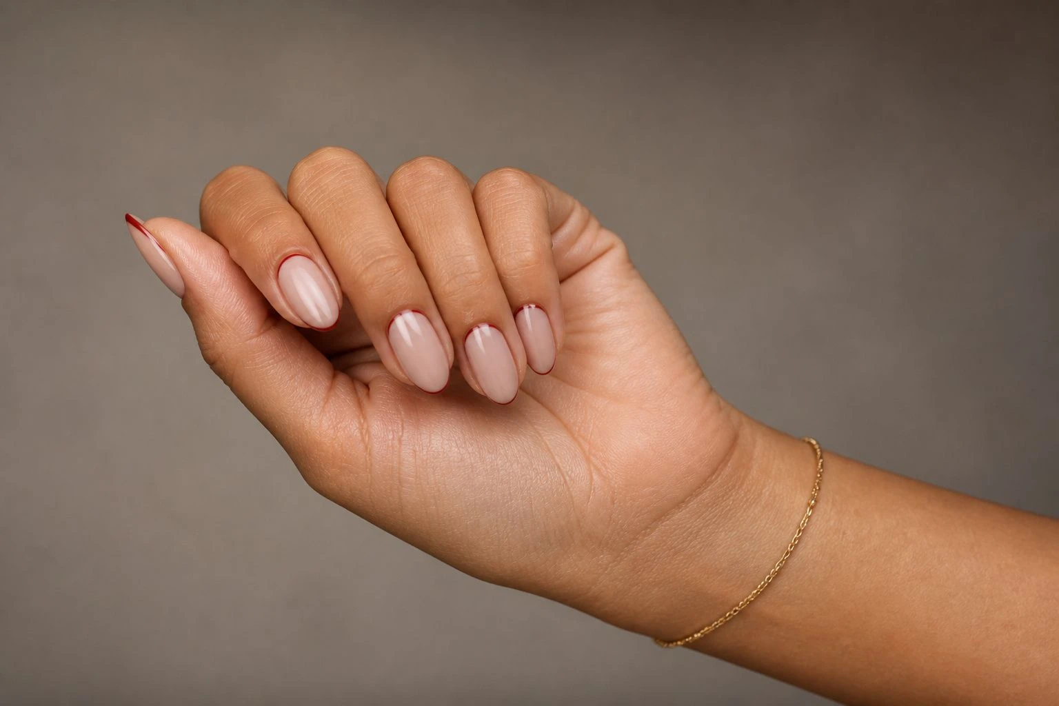 Sheer nude nails with a thin cranberry cuticle edge accent and a gold bracelet, simple Christmas nail idea