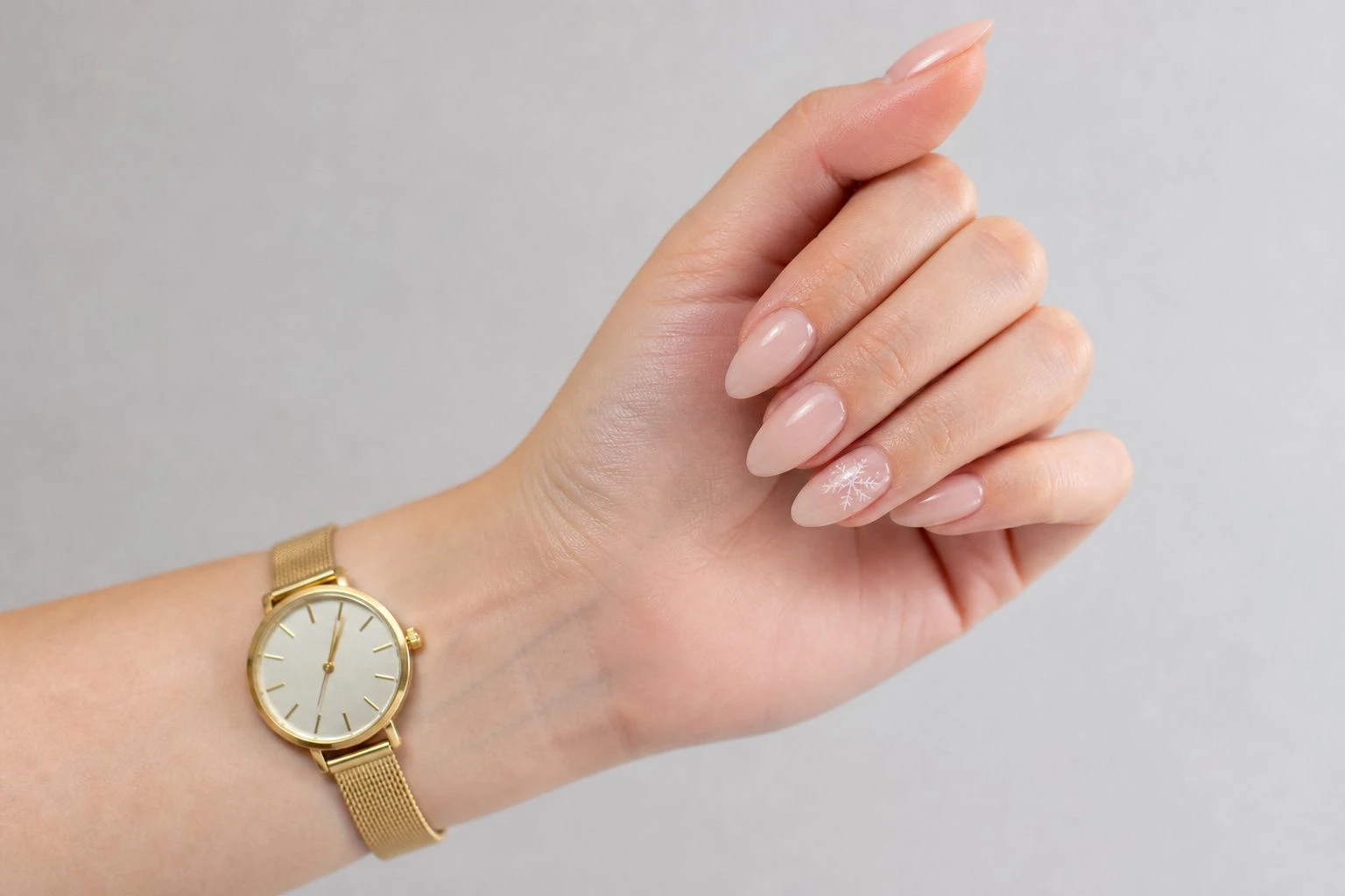 Sheer nude nails with a single white snowflake outline accent nail and a slim gold watch, simple Christmas nail idea