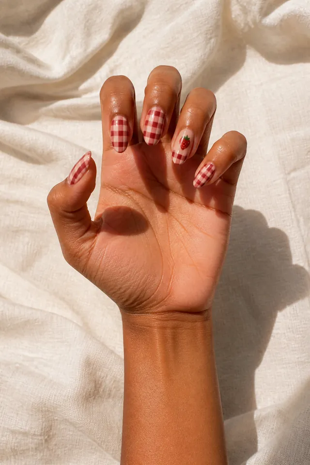 Strawberry gingham French accent on a sheer base, glossy finish, medium olive skin, hand lifted in natural window light with connected wrist