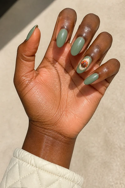 Sage green nails with framed turkey accent and gold dots, medium almond glossy pose, deep brown skin tone