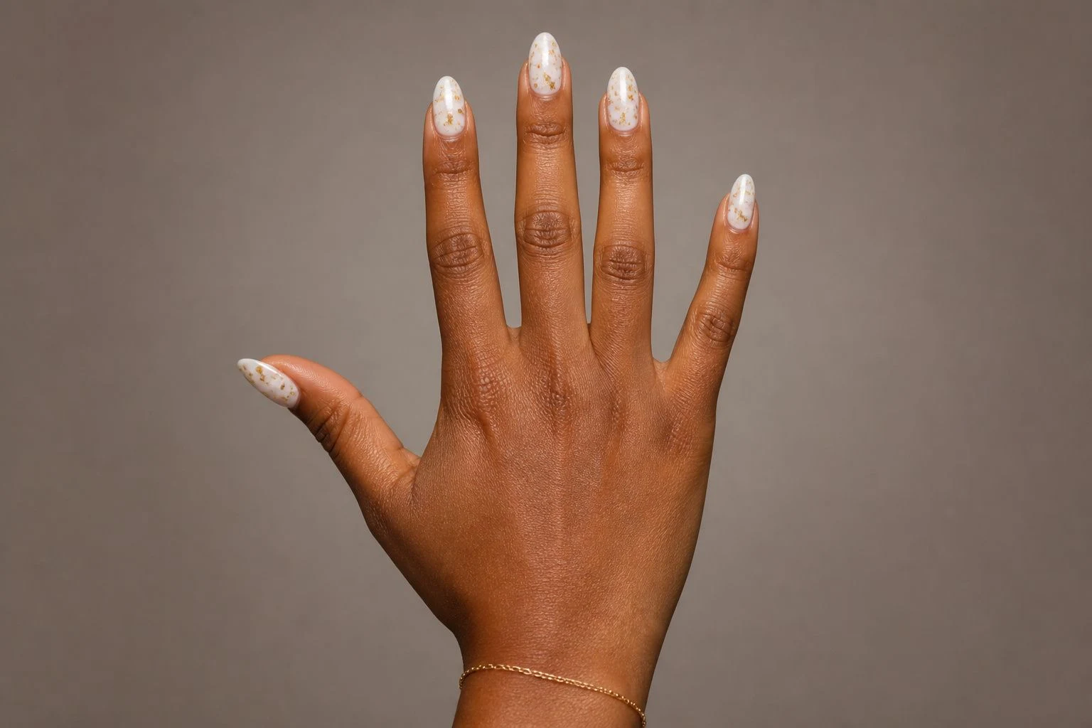 White Gel With Gold Foil Christmas nails with a delicate gold bracelet, all five fingers visible