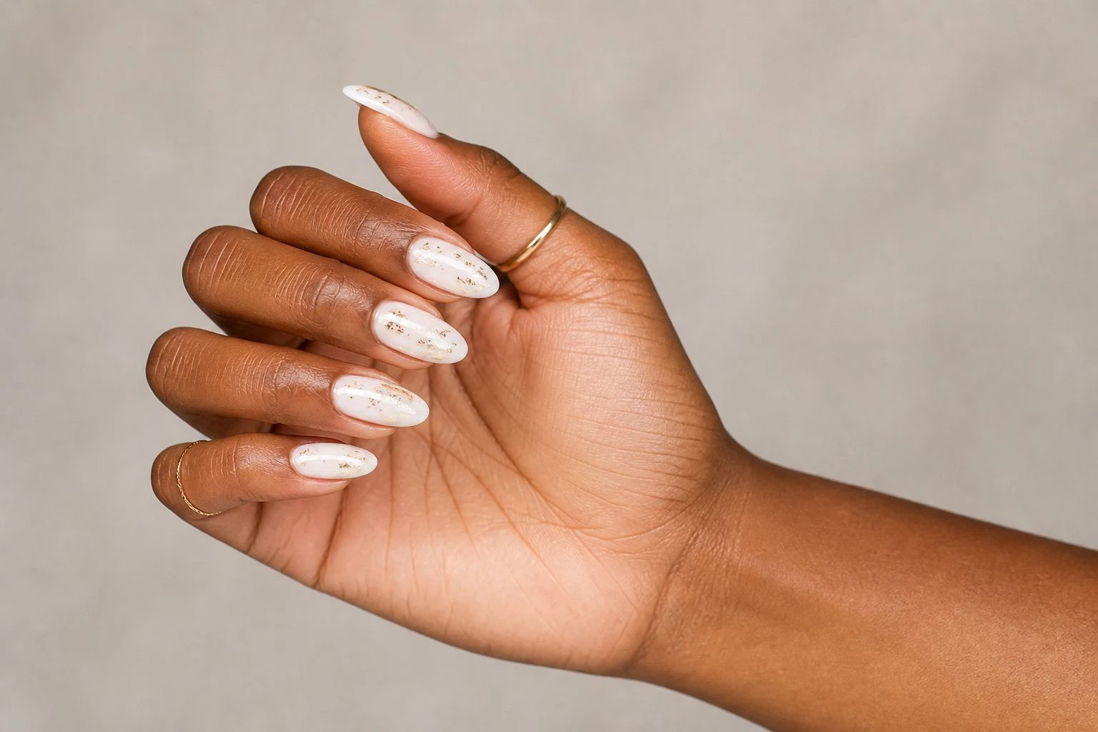 White nails with subtle gold foil and two thin gold rings, side profile pose