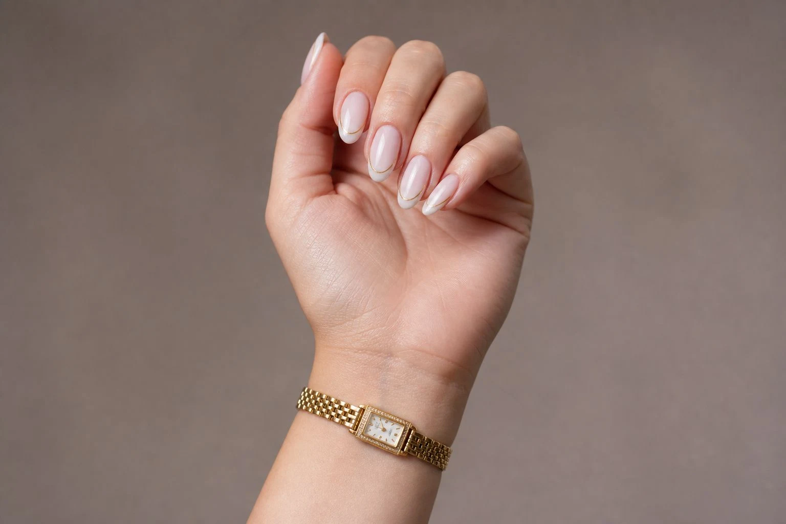 White micro French nails with a fine gold line in a curled hand pose with a delicate gold watch