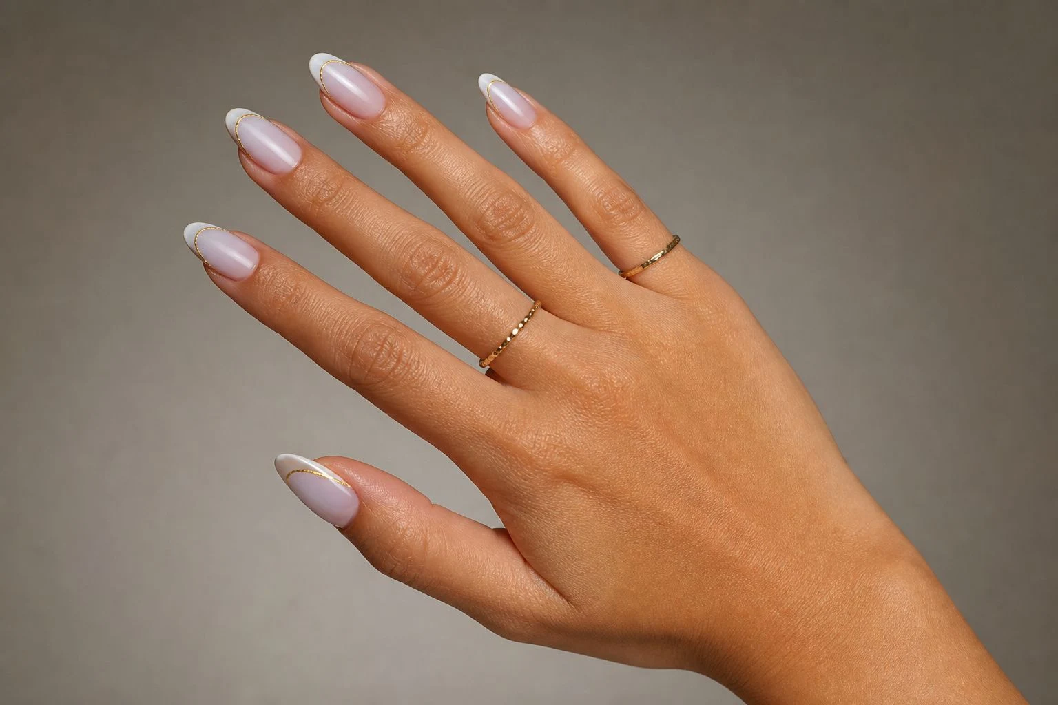 White micro French nails with a delicate gold line and two thin gold rings, natural fan pose