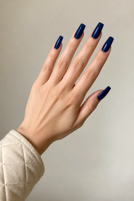 Glossy navy blue acrylic coffin nails on a relaxed diagonal hand pose with visible wrist, fair skin tone, soft daylight