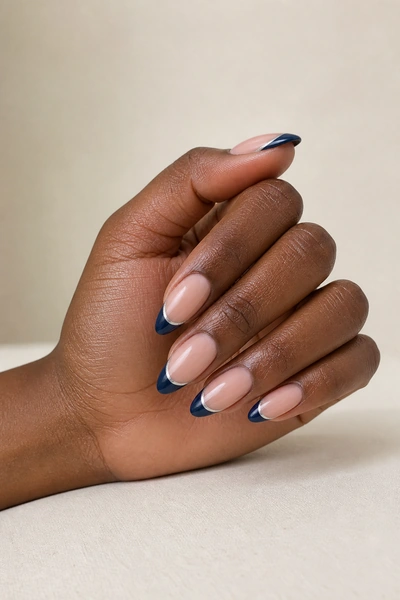 Navy acrylic French tips with a silver line on a fingertip-rest hand pose with visible wrist, deep brown skin tone, natural daylight