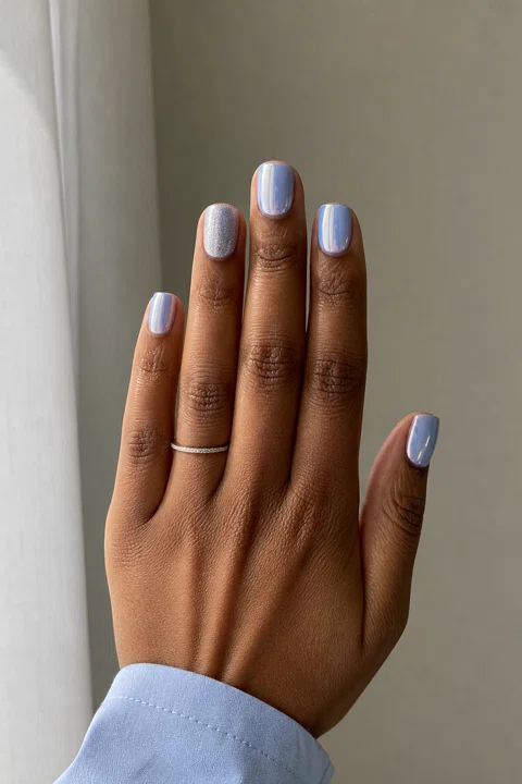 Icy blue chrome short squoval nails with a silver shimmer accent on a deep brown skin tone, shown on one upright fan hand with a pale blue cuff and connected short wrist
