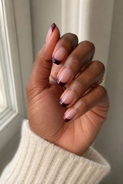 Crisp white French tip nails on a deep brown skin tone hand in a side angled display with visible wrist and short partial forearm, natural daylight