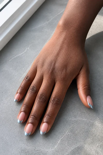 Icy blue chrome French tip nails on a deep brown skin tone hand in a fingertip-rest pose with visible wrist and short partial forearm, natural daylight