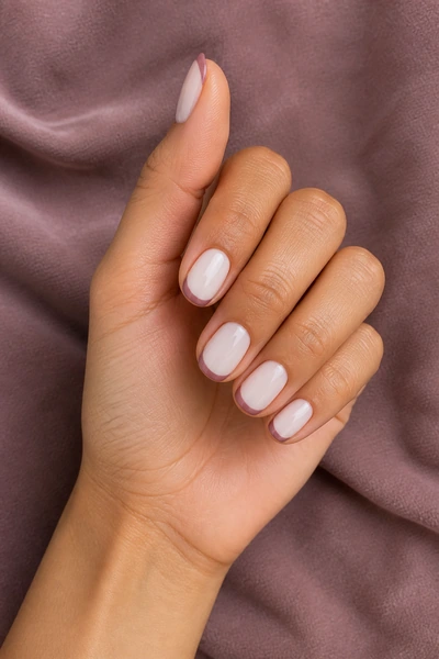 Dusty mauve French tip nails on a light brown skin tone hand in a gentle pinch pose with visible wrist and short partial forearm, natural daylight