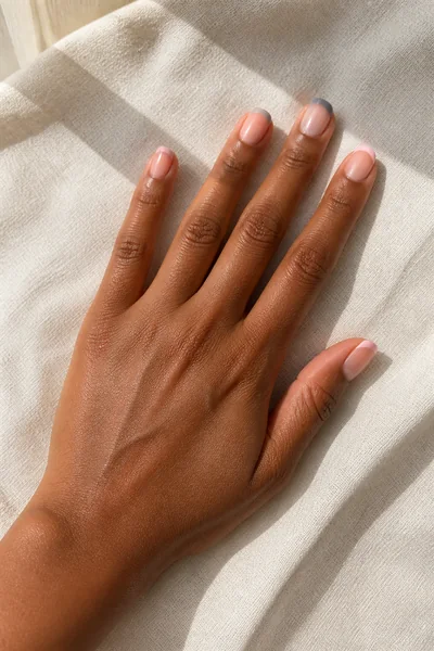Blush and soft grey French tip nails on a fair skin tone hand in a relaxed fingertip display with visible wrist and short partial forearm, natural daylight
