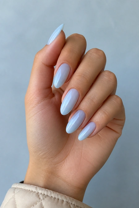 Icy blue almond nails on a light olive skin tone hand in a fingertip-rest pose with visible wrist and short partial forearm, natural daylight