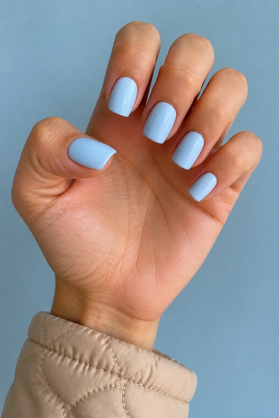Pale blue glossy square nails on a tan skin tone hand in an open palm angle with visible wrist and short partial forearm, natural daylight