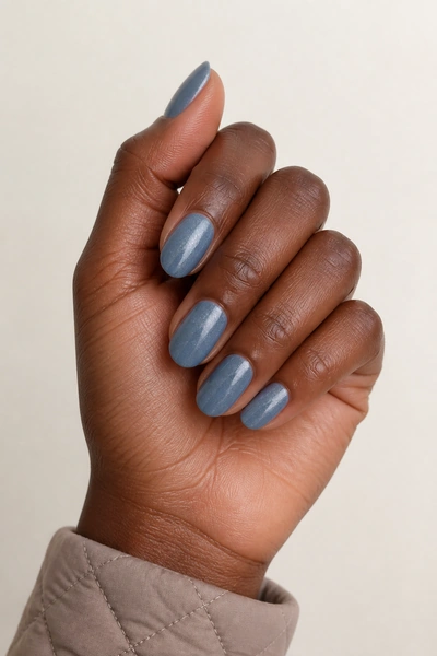 Dusty blue shimmer oval nails on a rich dark brown skin tone hand in a gently crossed pose with visible wrist and short partial forearm, natural daylight