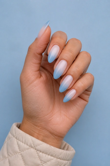 White and icy blue ombre nails on a light brown skin tone hand in a fingertip-rest pose with visible wrist and short partial forearm, natural daylight