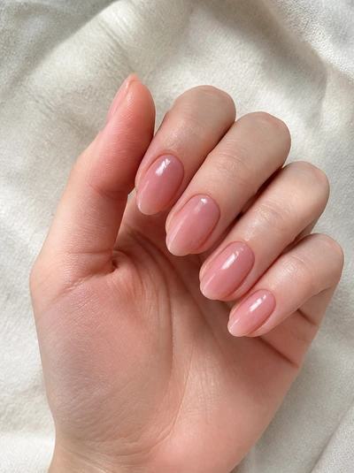 Sheer rosewater nude almond nails with a glossy finish on a fair skin tone hand in a softly curled pose with a cream sleeve and visible wrist