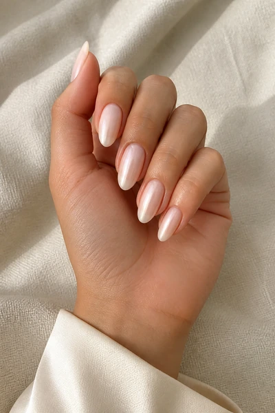 Milky pearl almond nails on a light olive skin tone hand in a compact curled pose with a satin ivory cuff and soft natural light