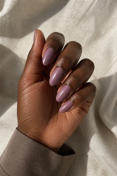 Muted mauve satin almond nails on a rich dark brown skin tone hand in a softly curled pose with a taupe knit cuff and visible wrist