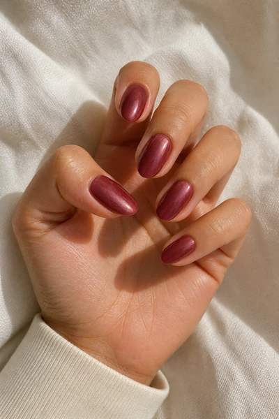 Glazed berry almond nails on a medium olive skin tone hand in a relaxed curled pose with a cream textile cuff and soft daylight