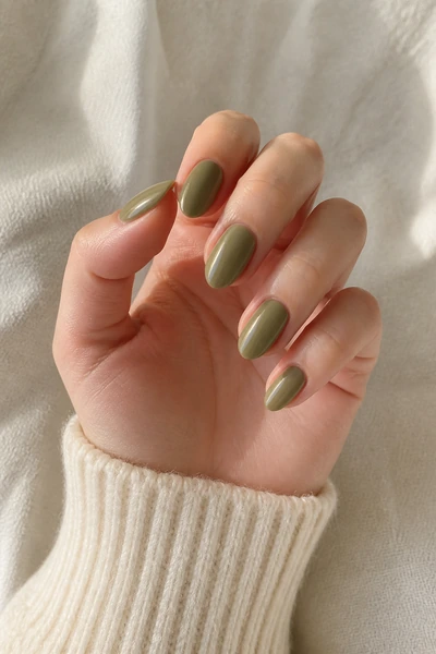 Muted olive green almond nails with a glossy finish on a fair skin tone hand in a softly curled pose with a cream sleeve and visible wrist