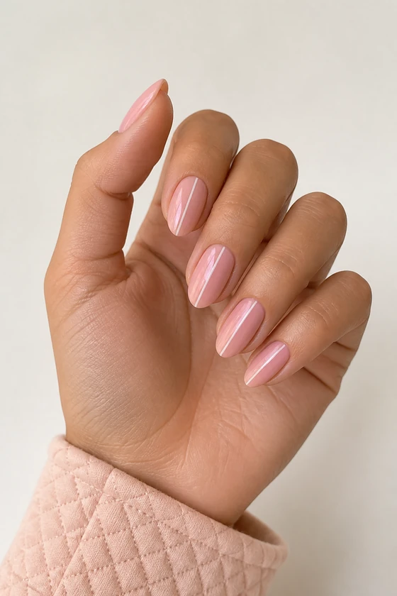 Fair skin hand in a compact curled pose wearing glossy blush-pink almond nails with fine ivory ribbon lines and a pink quilted cuff